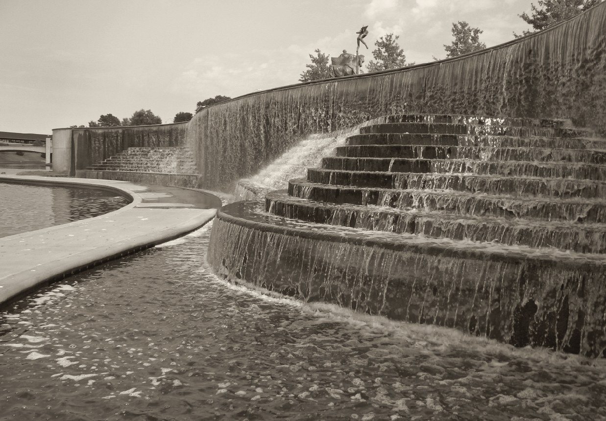 Warm-toned black and white print of the Volker fountain, water running down a long curved flight of stone steps into a still basin.