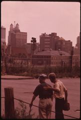 Two men from behind at a guardrail on an empty street, the skyline beyond.