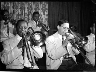 Two trombone players in white jackets with their slides crossed, trumpets behind.